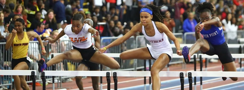 Female hurdlers clear a hurdle during the 2019 Class 4A State Indoor Meet.